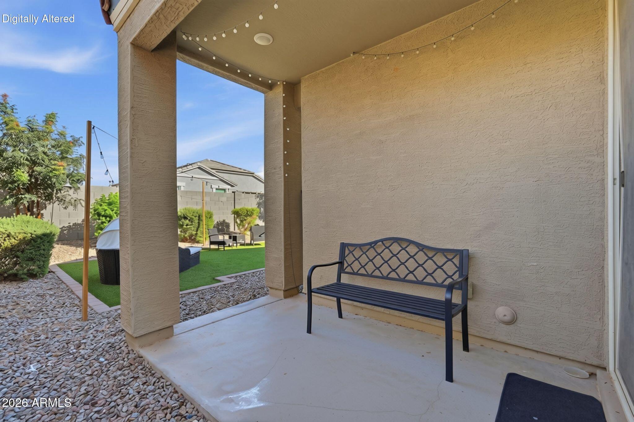 Covered patio with a metal bench and string lights overlooking an artificial turf backyard.