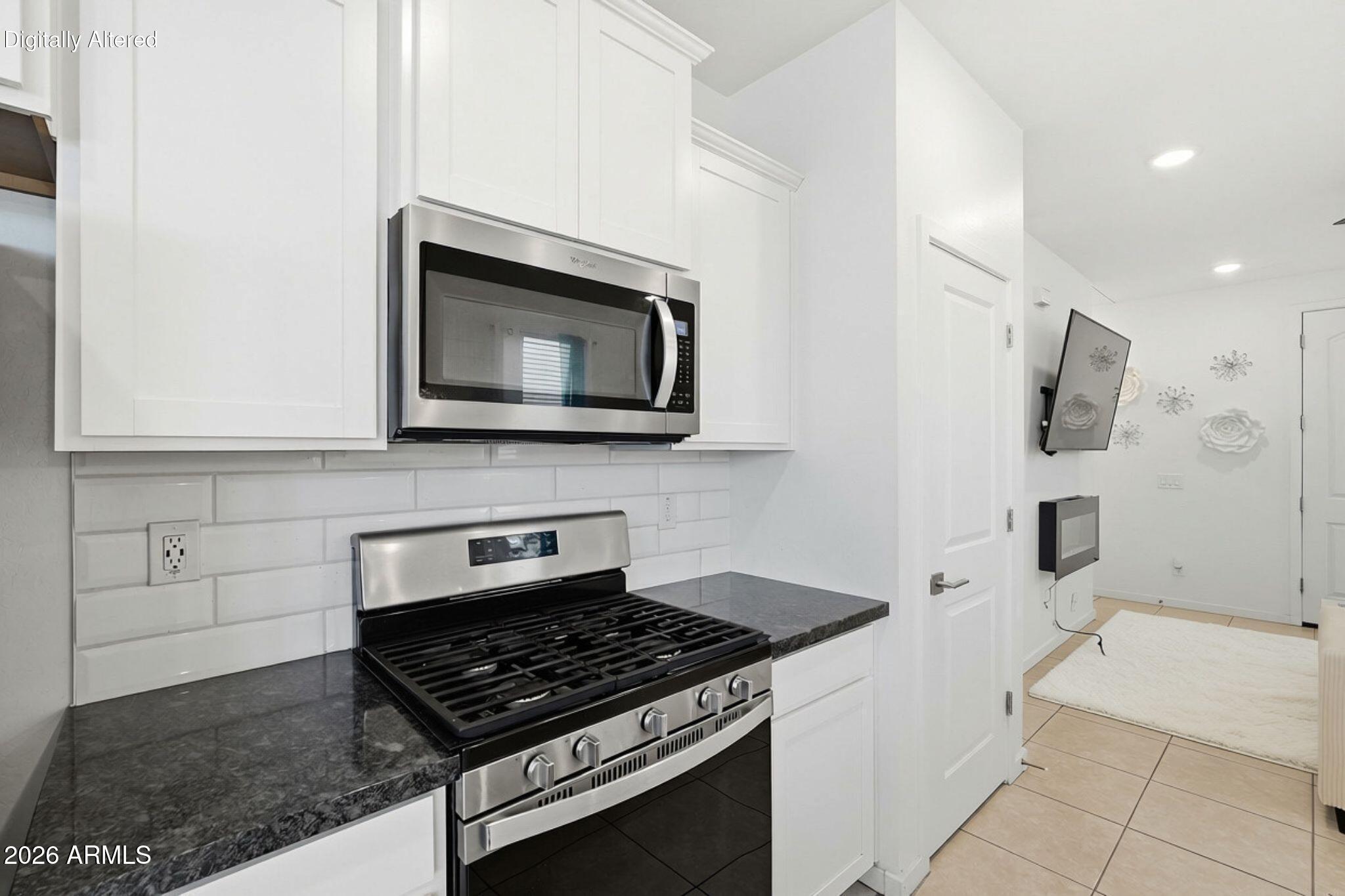 Kitchen with white cabinetry, dark countertops, and a stainless steel gas range and microwave.