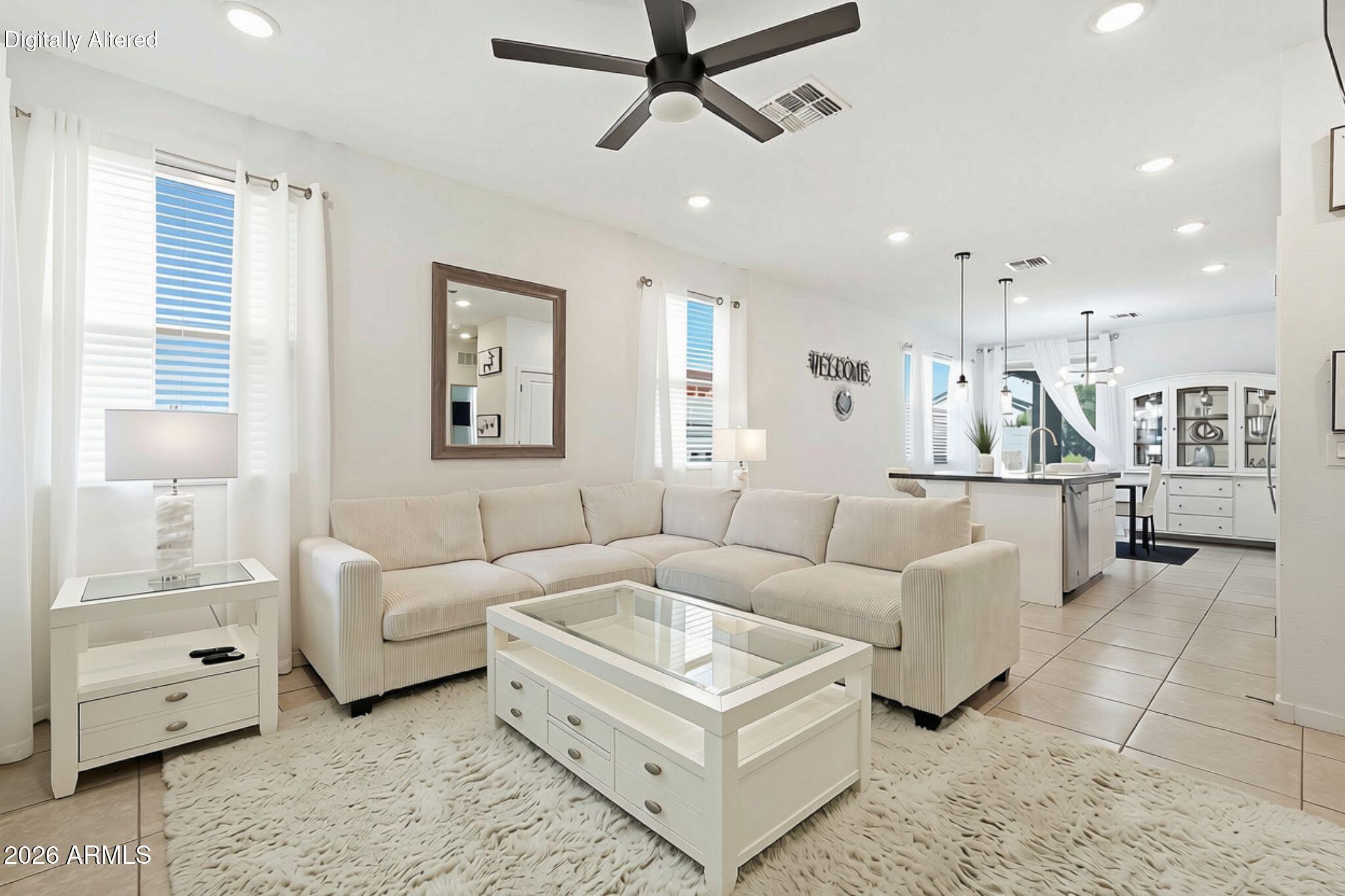 Furnished living room with cream sectional and glass coffee table, opening to a bright kitchen.