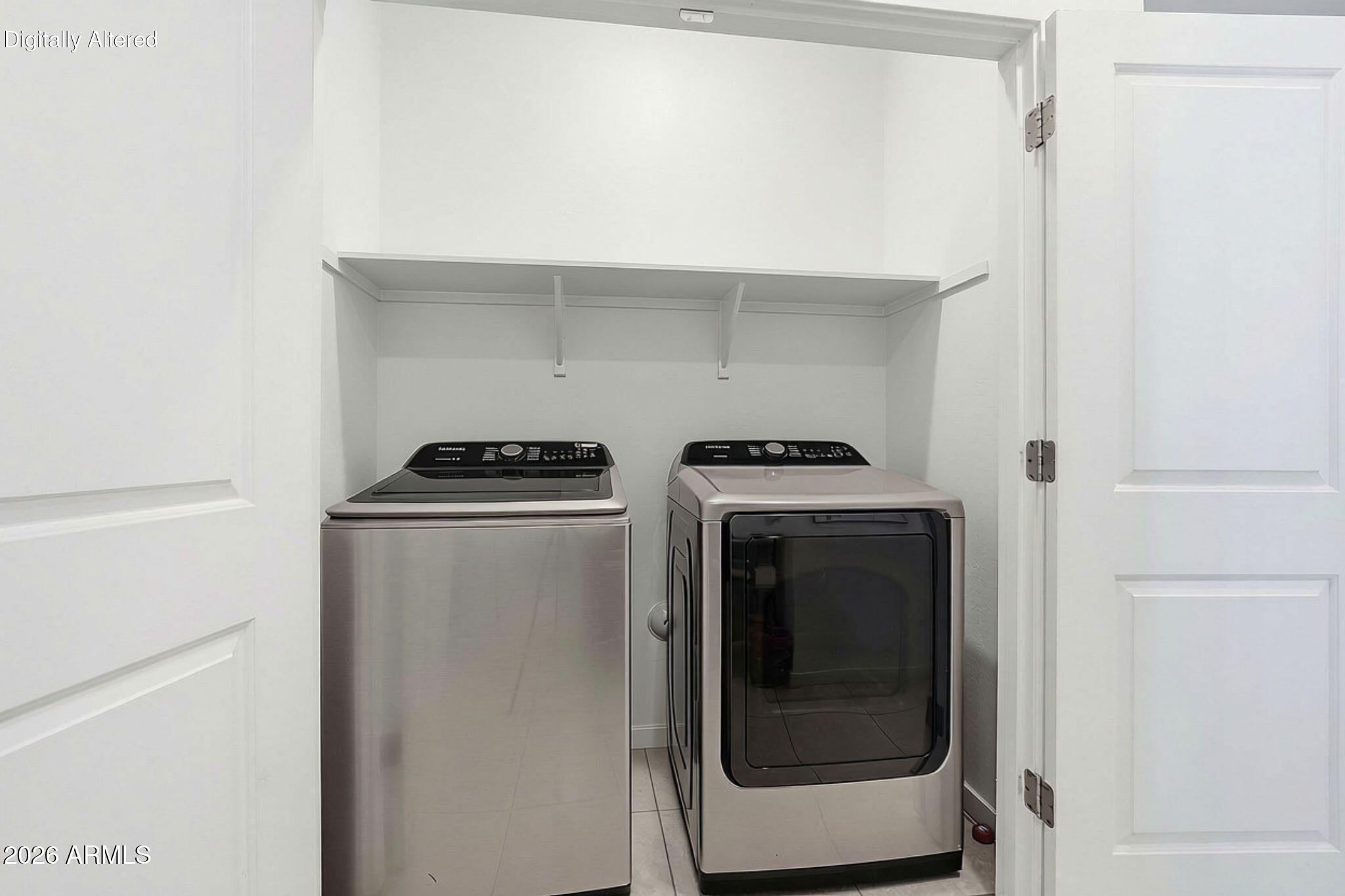 Laundry room with stainless steel washer and dryer beneath a white storage shelf.