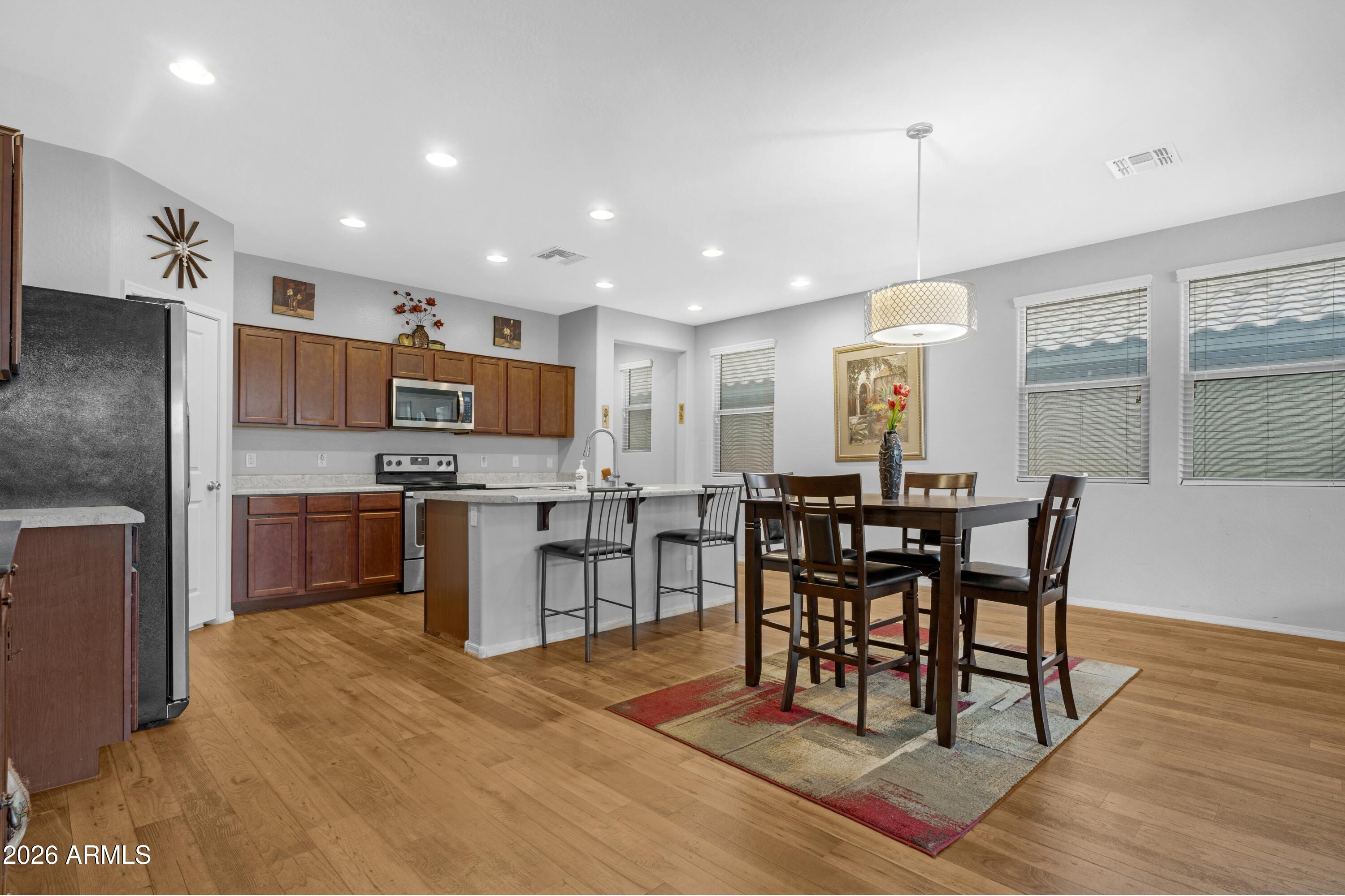 Open kitchen and dining area with wood cabinets, breakfast island, and dining table on a patterned rug.
