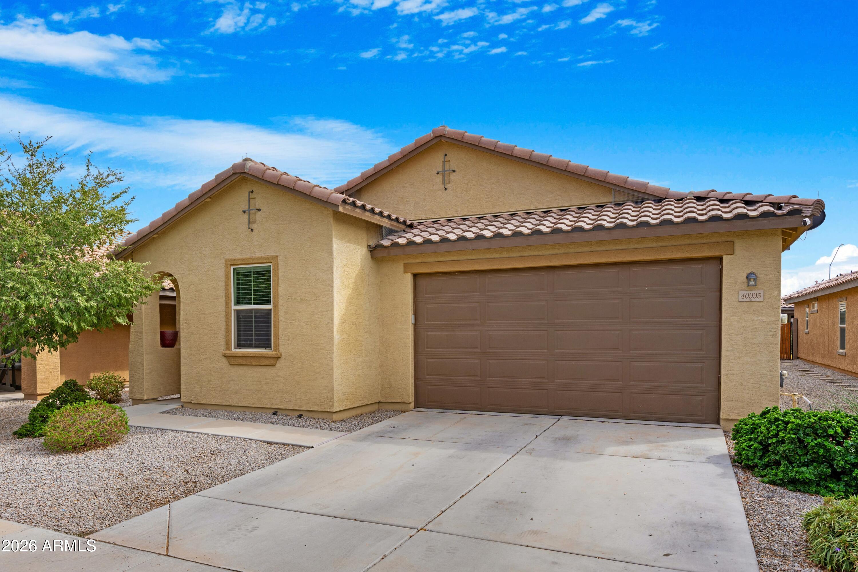 Tan stucco home with a tiled roof, double garage, and desert gravel landscaping.