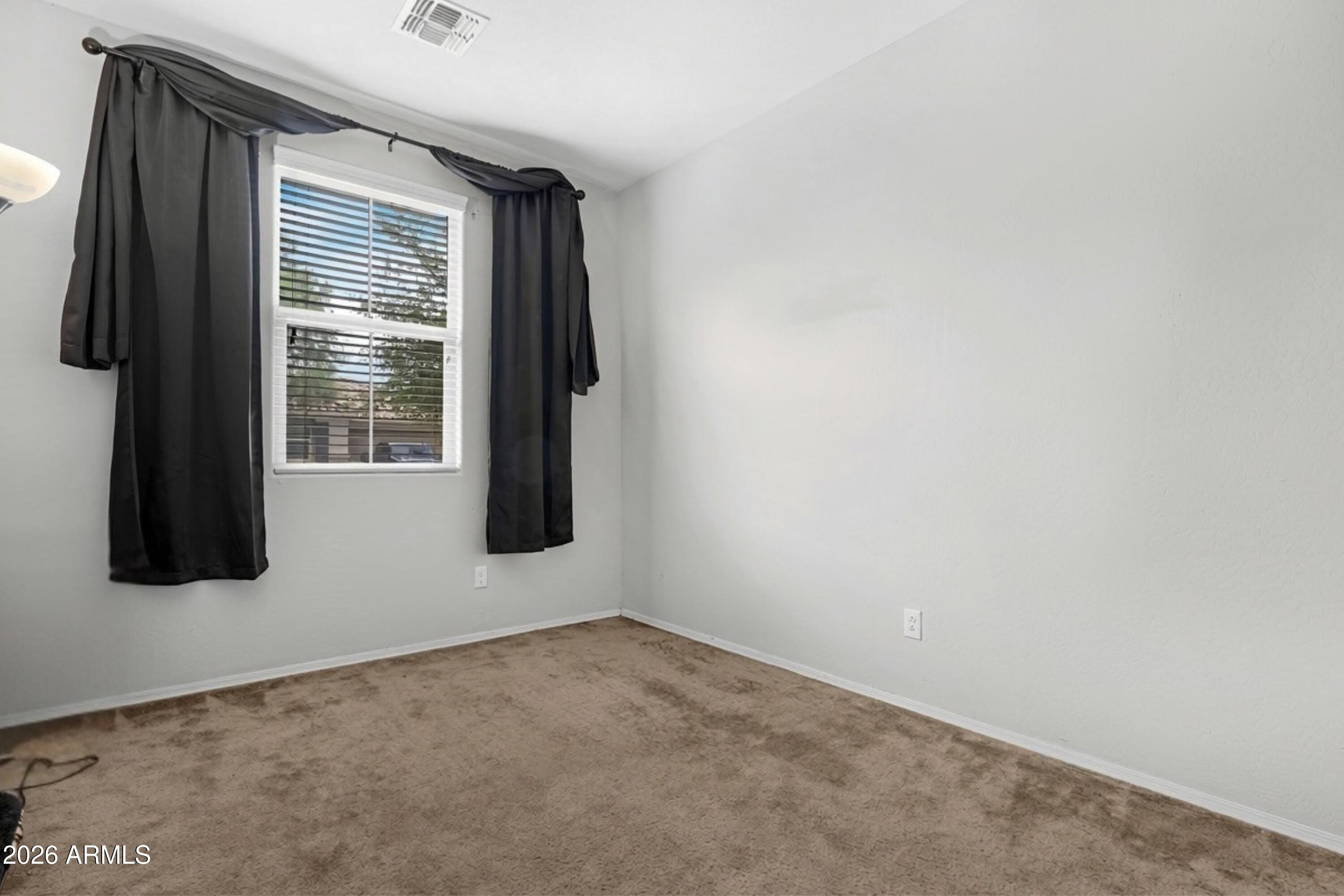 Empty bedroom with beige carpet and a window framed by dark curtains.