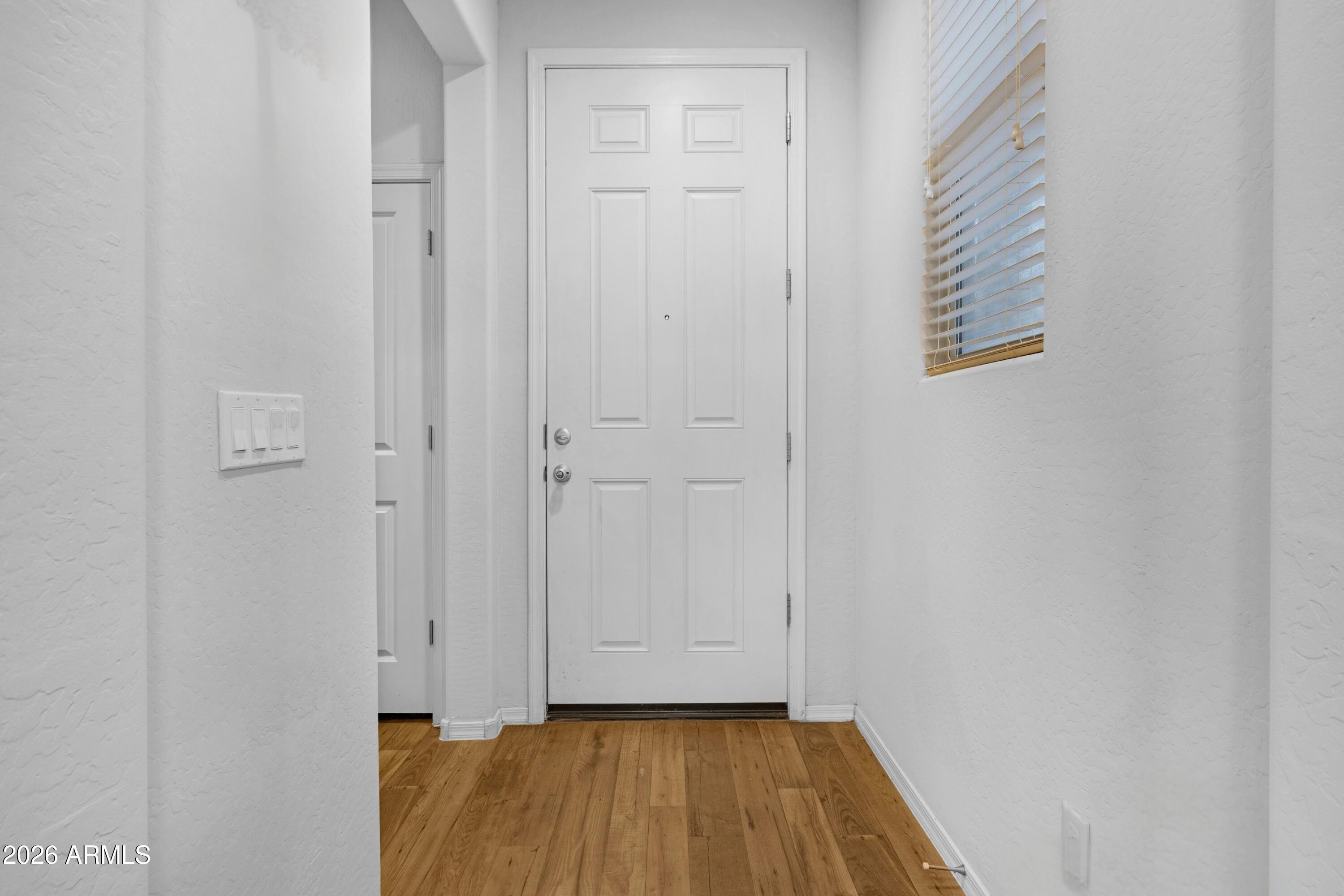 Entryway with a white paneled front door, wood-look flooring, and a window with blinds.