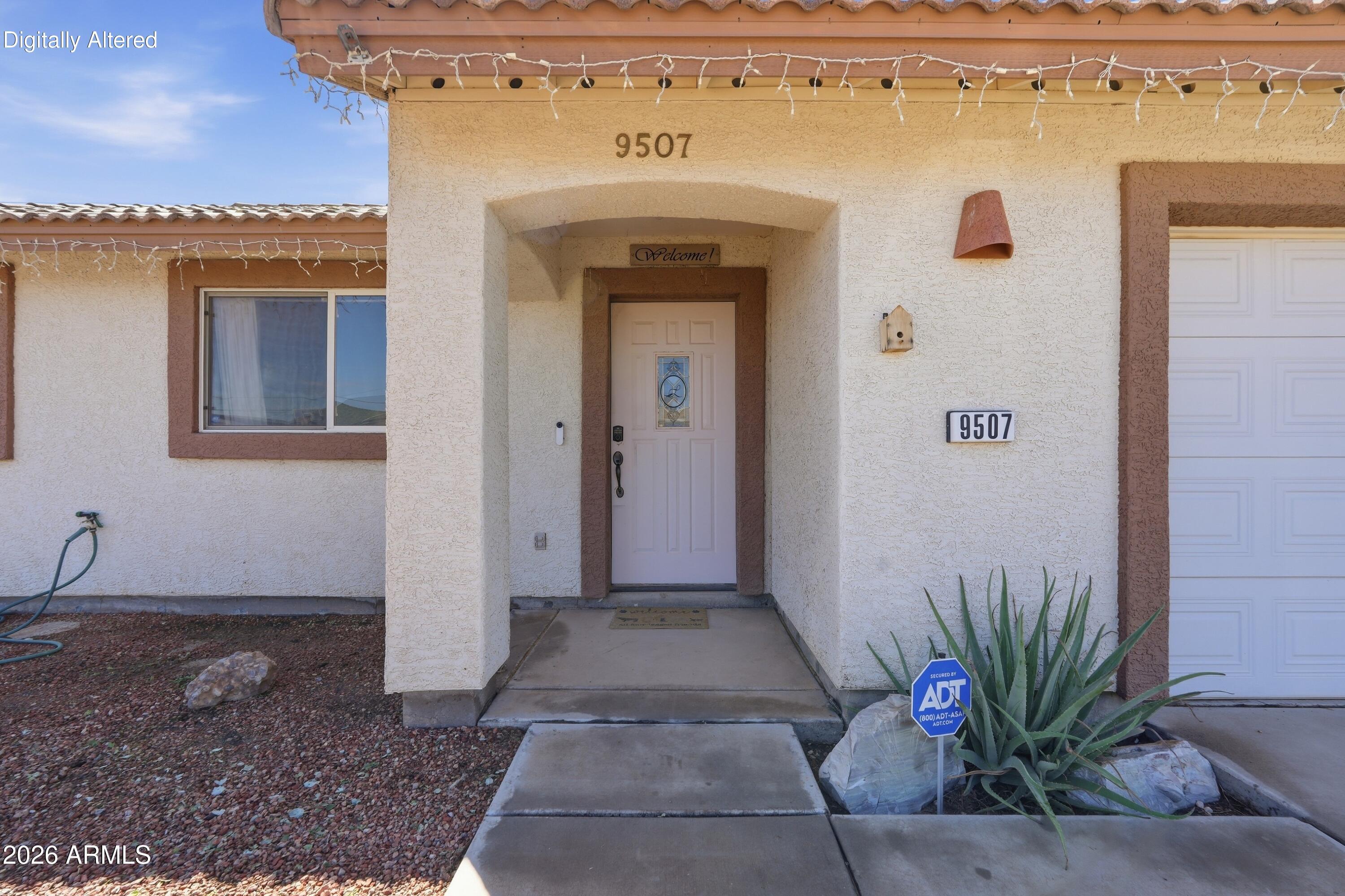Home entrance with recessed white door, tiled roof, string lights, and desert landscaping.