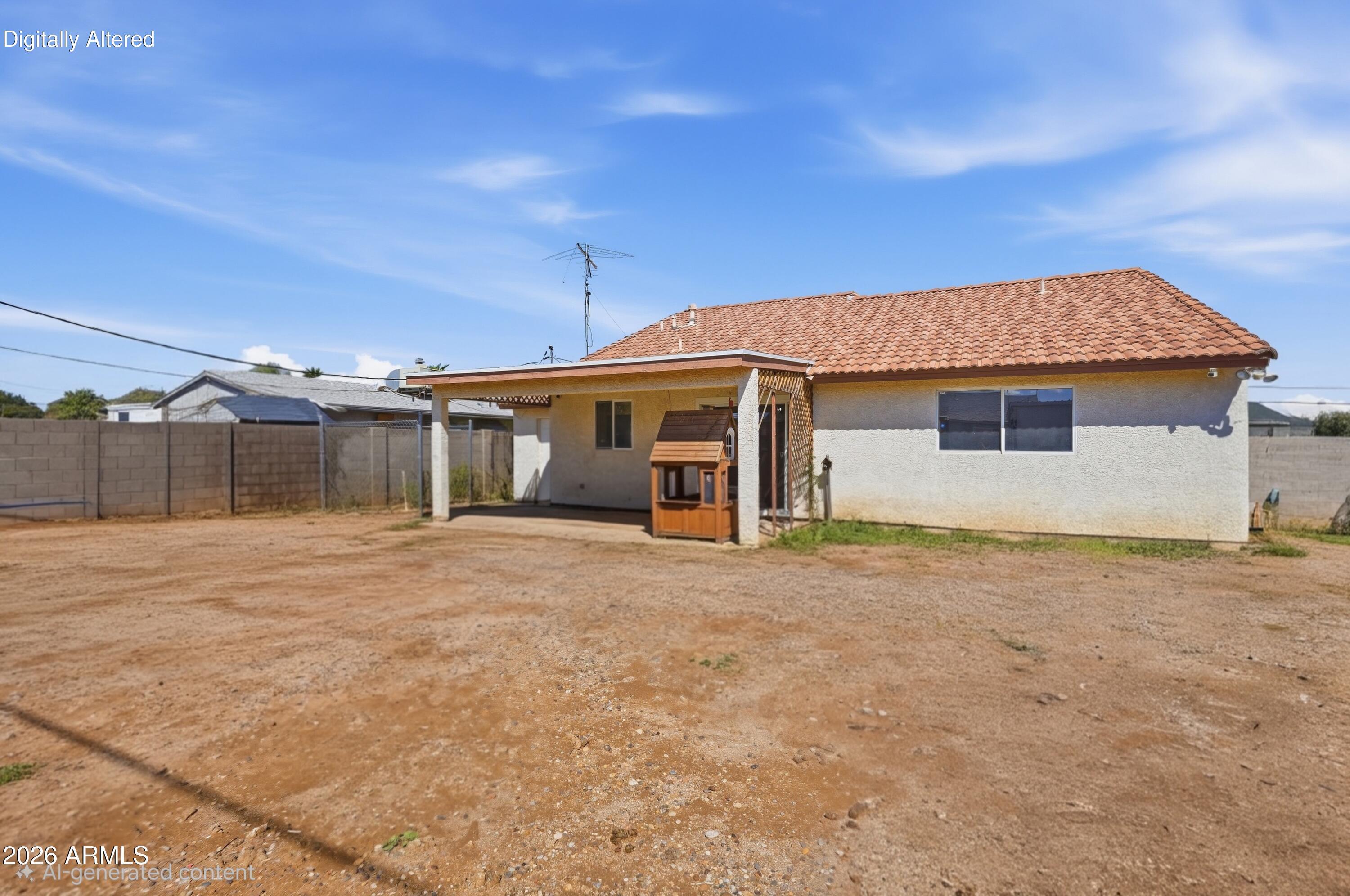 Rear of a stucco home with a covered patio, tile roof, and wide dirt backyard.