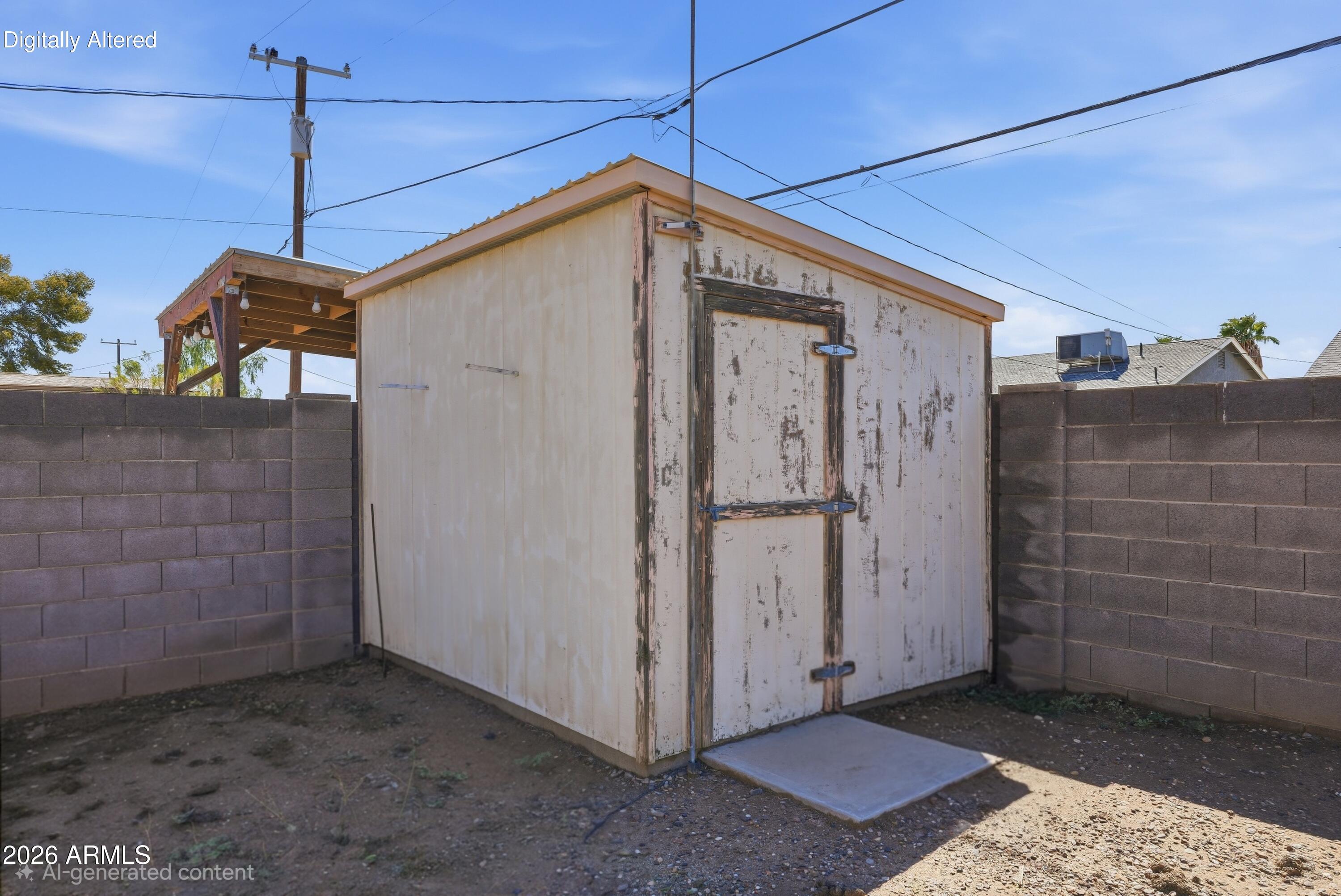 Weathered white storage shed in a fenced dirt yard, with a concrete entry pad.