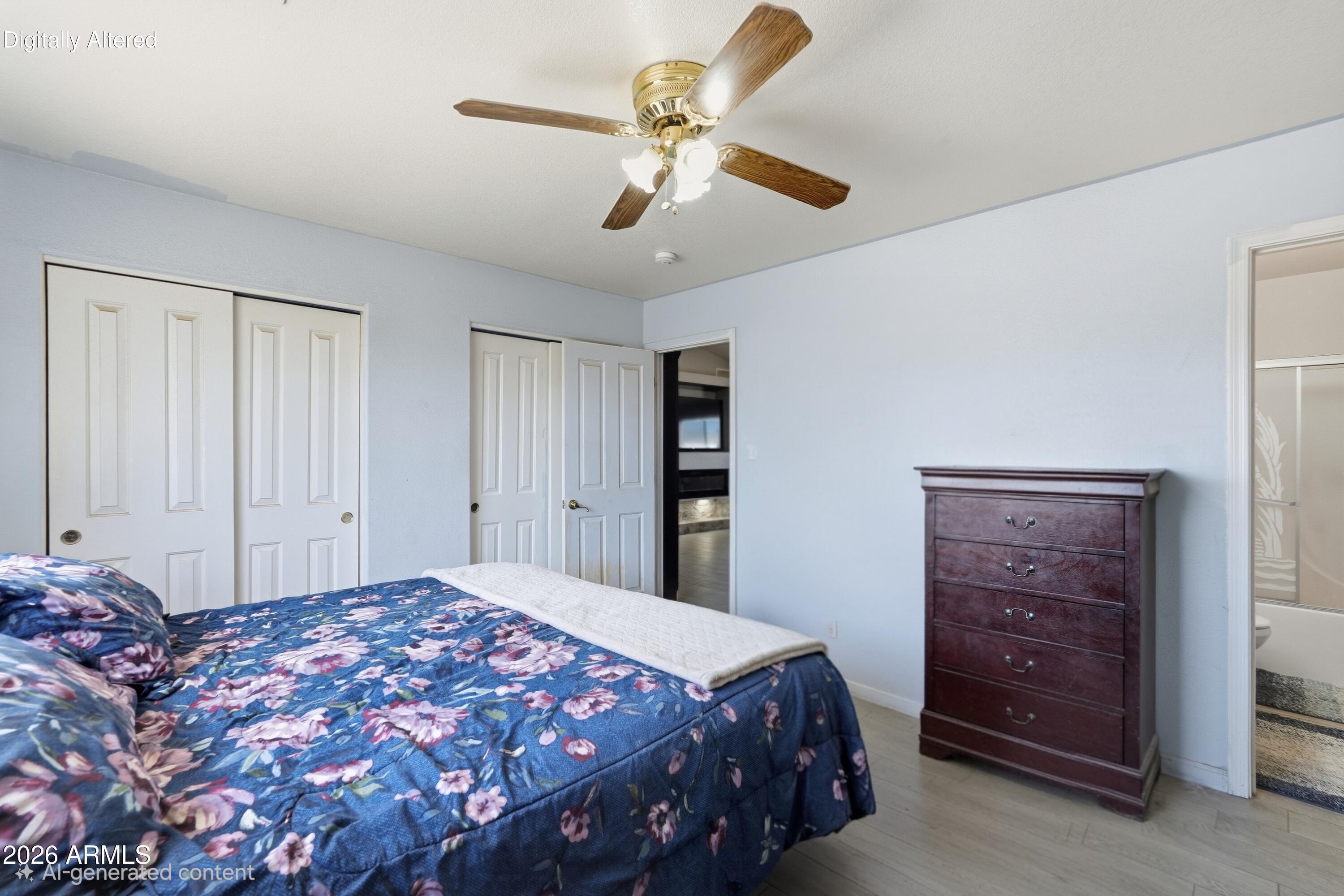 Furnished bedroom with a blue floral bedspread, ceiling fan, sliding closets, and dark wood dresser.