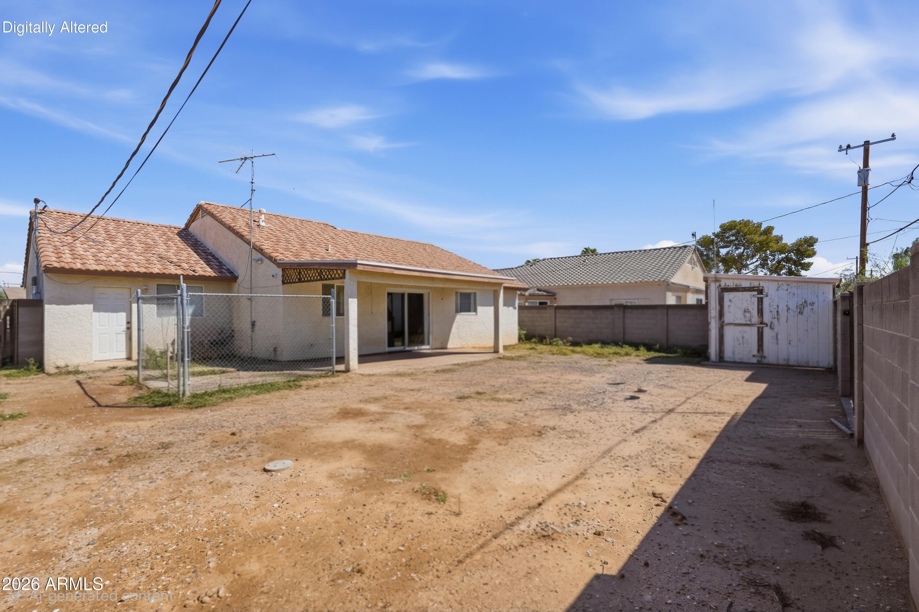 Home’s rear exterior with a covered patio, bare dirt backyard, block walls, and a weathered shed.