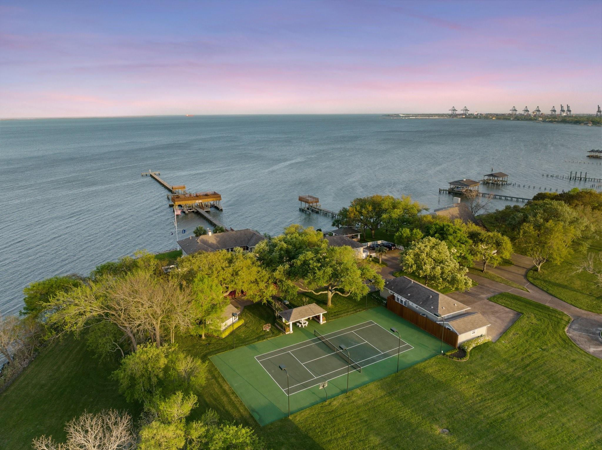 Waterfront property with a tennis court, tree-shaded homes, and piers extending into the bay.