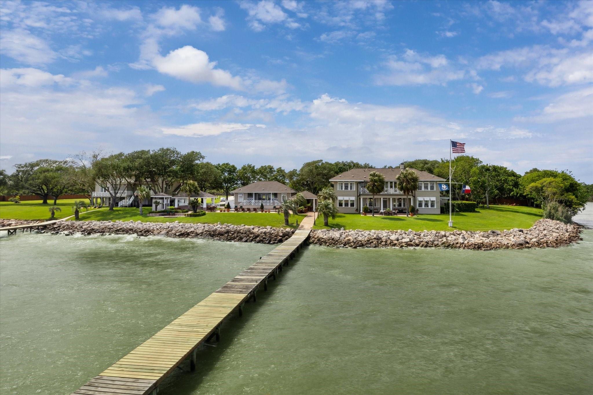 Waterfront homes and green lawn with a long wooden dock extending across the water.