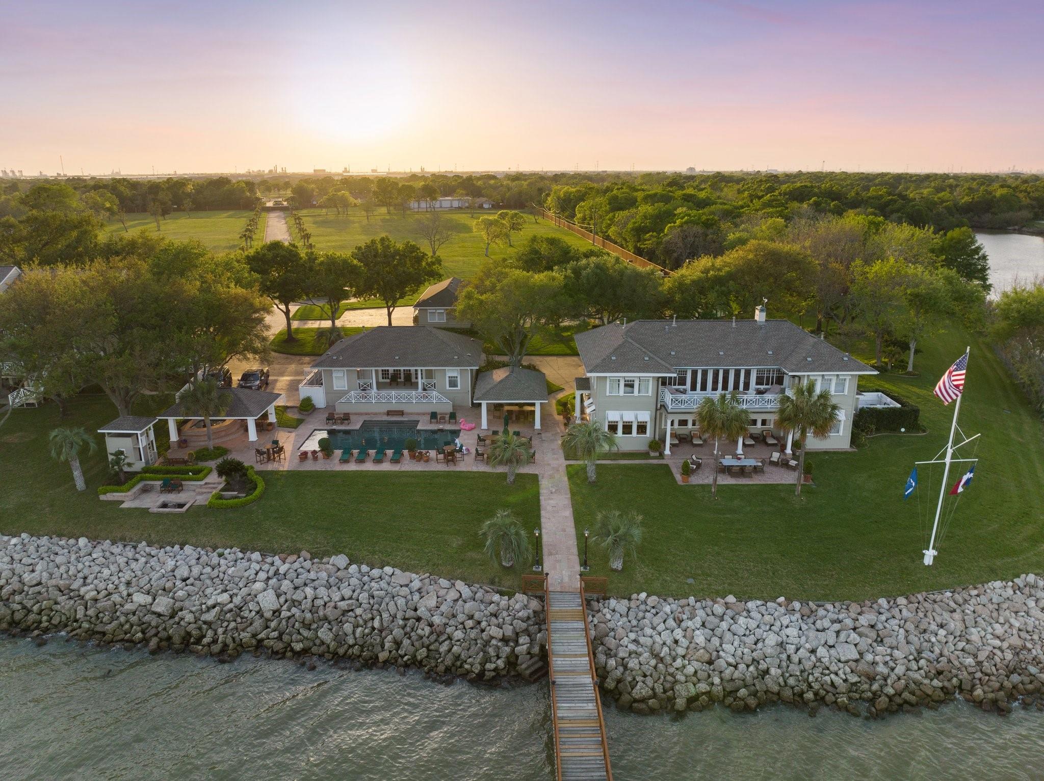Waterfront home with a pool, landscaped grounds, and a dock along a rocky shoreline.