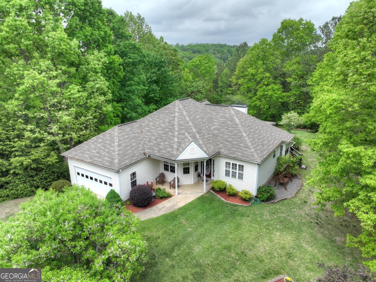 White one-story home with a broad gray roof, attached garage, and landscaped lawn surrounded by mature trees.