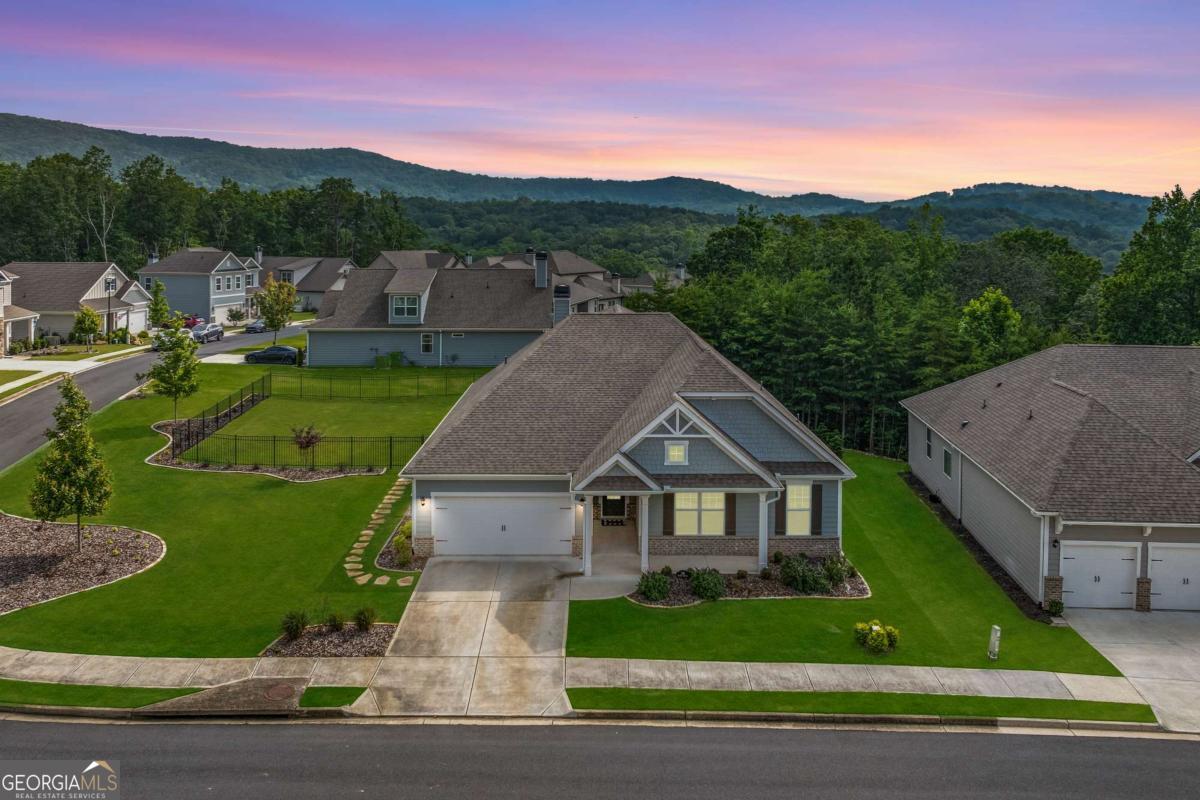 Gray house with a two-car garage and lawn, backed by wooded hills at dusk.