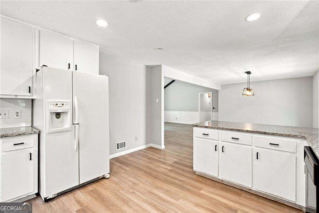 Kitchen with white cabinets, a refrigerator, and a granite-topped island opening to a hardwood-floored room.