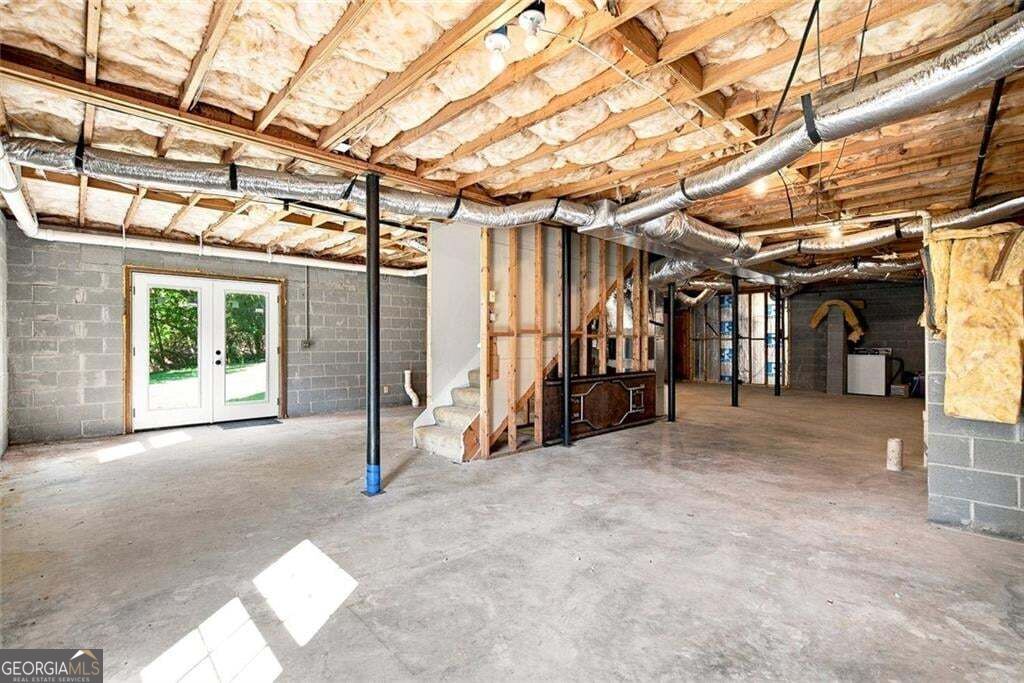 Unfinished basement with exposed framing, insulated ceiling, concrete floor, and French doors.
