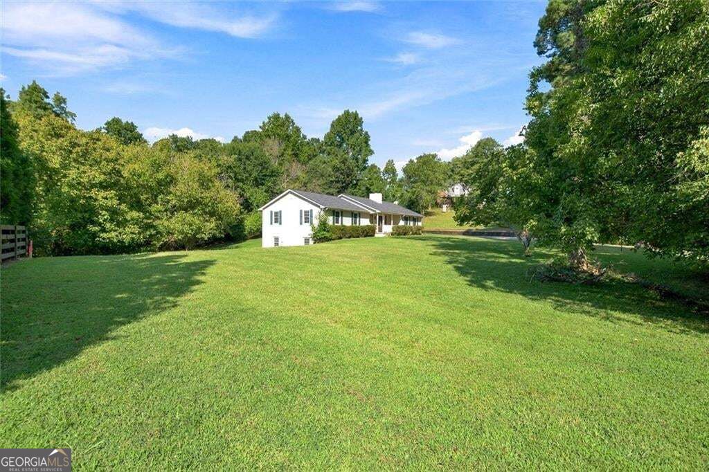 White ranch-style home beyond a broad lawn, framed by mature trees.