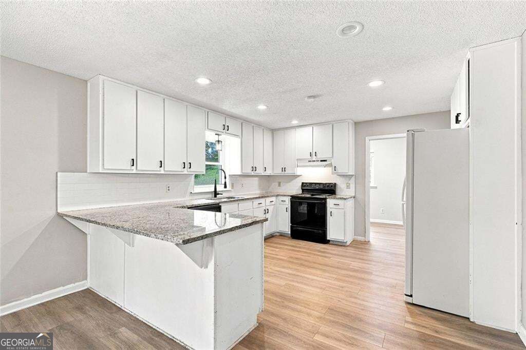 Kitchen with white cabinets, granite peninsula, black range, and wood-look flooring.