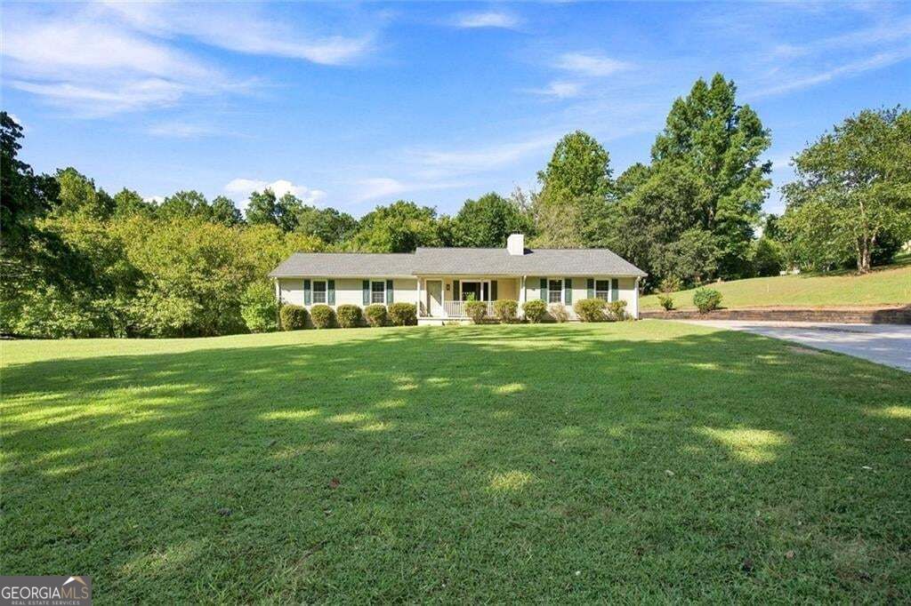 Single-story home beyond a broad lawn, with a front porch and mature trees.