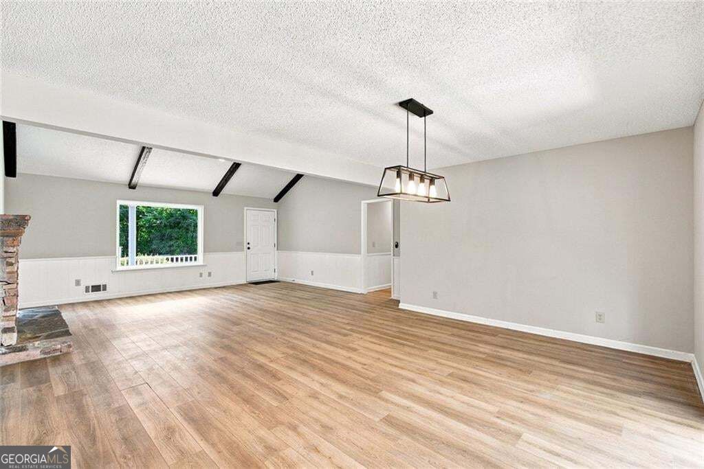 Empty living room with wood flooring, exposed ceiling beams, and a hanging light fixture.