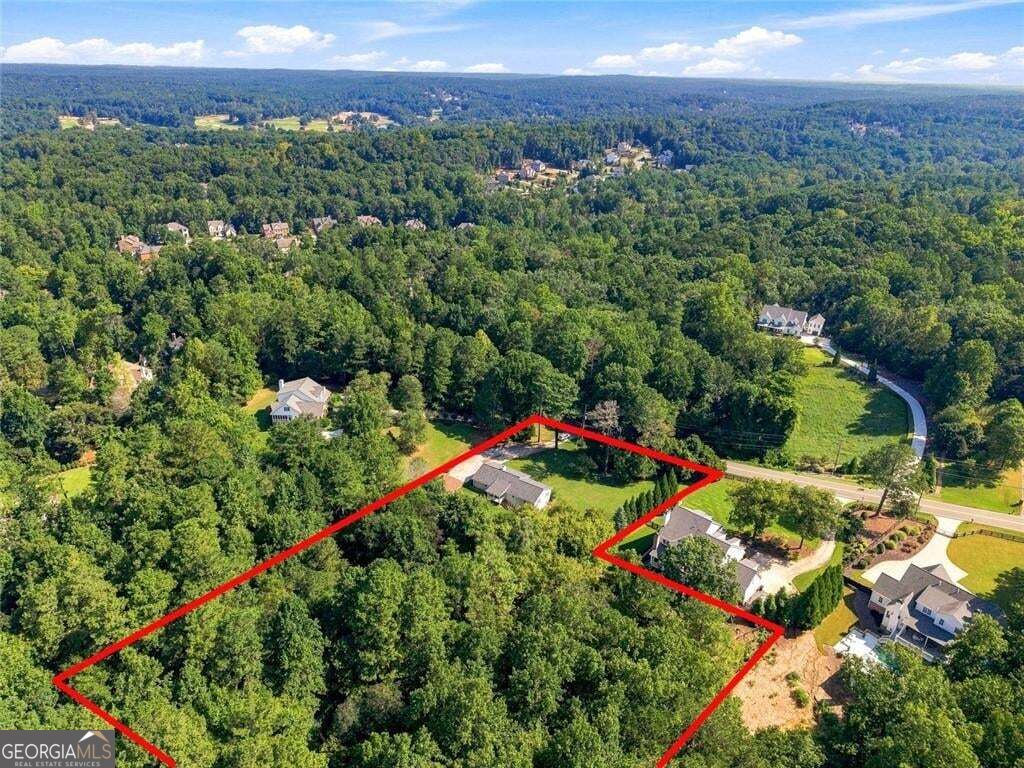 Aerial view of a wooded property outlined in red beside a residential road.