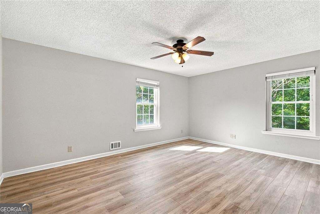 Empty room with gray walls, wood-look flooring, two windows, and a ceiling fan.