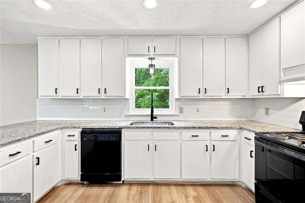 Bright kitchen with white cabinets, granite counters, a window above the sink, and black appliances.