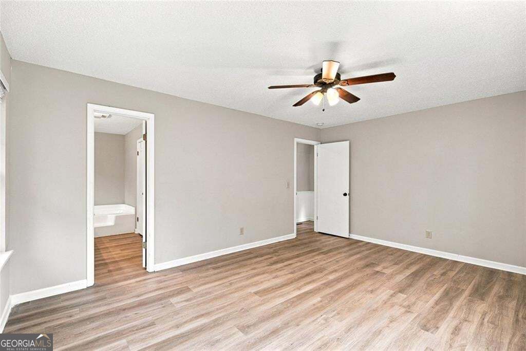 Empty bedroom with wood-look flooring, a ceiling fan, and two open doorways.