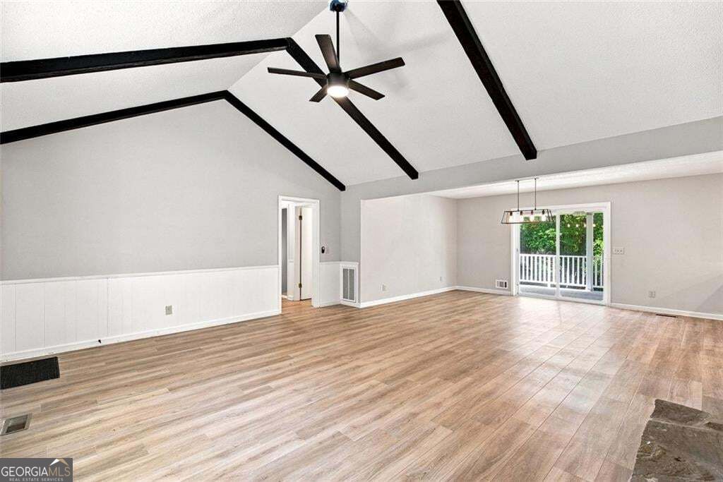 Vacant living room with vaulted beamed ceiling, ceiling fan, and sliding doors to a deck.