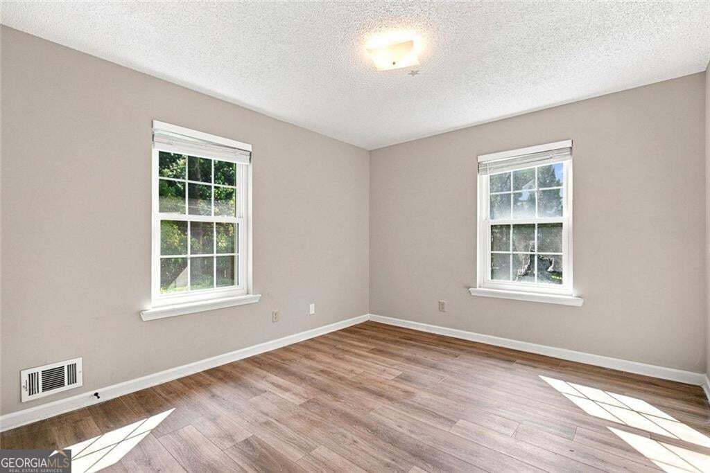 Empty room with wood-look flooring, two windows, and neutral walls.