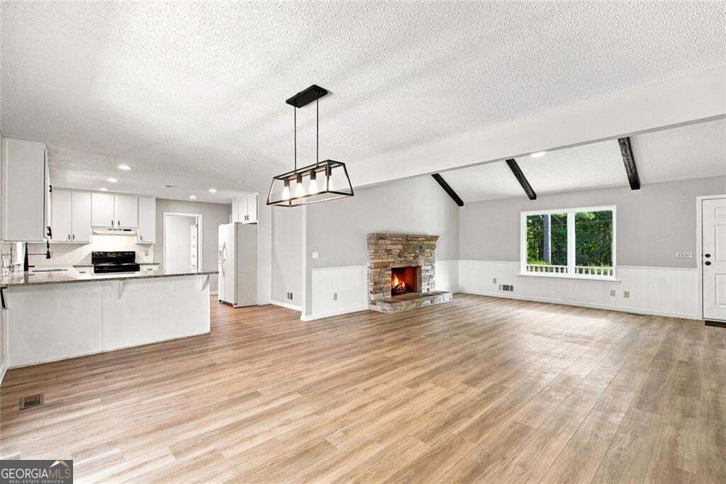 Open kitchen and living room with wood flooring, exposed ceiling beams, and a stone fireplace.