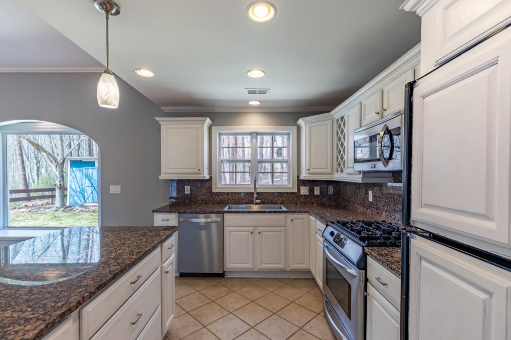 Kitchen with white cabinets, granite counters, stainless steel appliances, and a window above the sink.