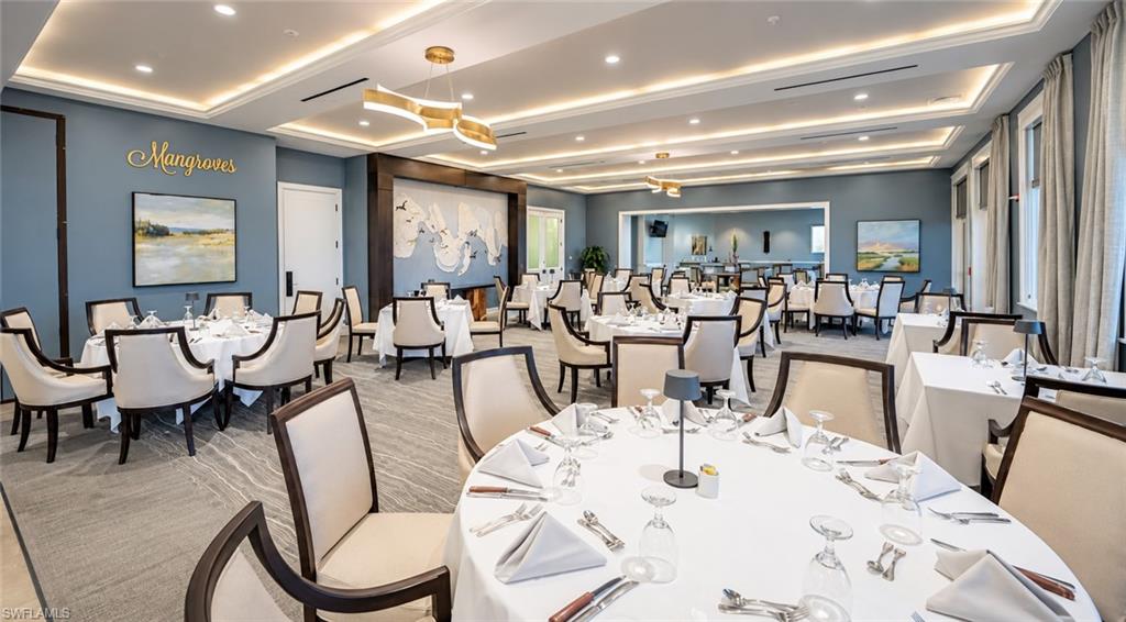 Furnished dining room with white-clothed tables, upholstered chairs, and a decorative recessed ceiling.
