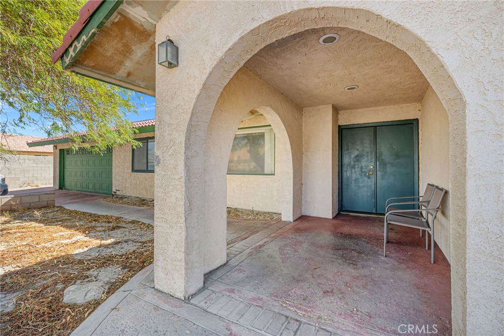 Home exterior with an arched covered entry, green front door and garage door, and a chair on the porch.