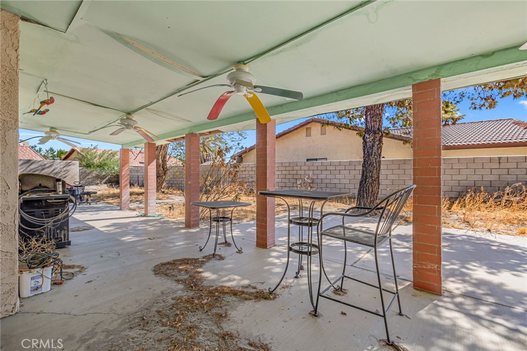 Covered backyard patio with ceiling fans, brick columns, outdoor dining set, and barbecue grill.