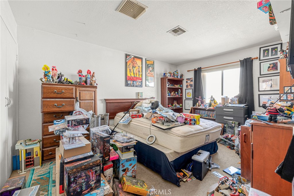 Bedroom crowded with collectible figures, toys, and boxes around a bed and display shelves.