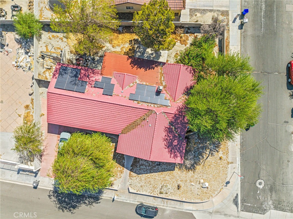 Aerial view of a red-tile-roof home with solar panels on a tree-lined corner lot.