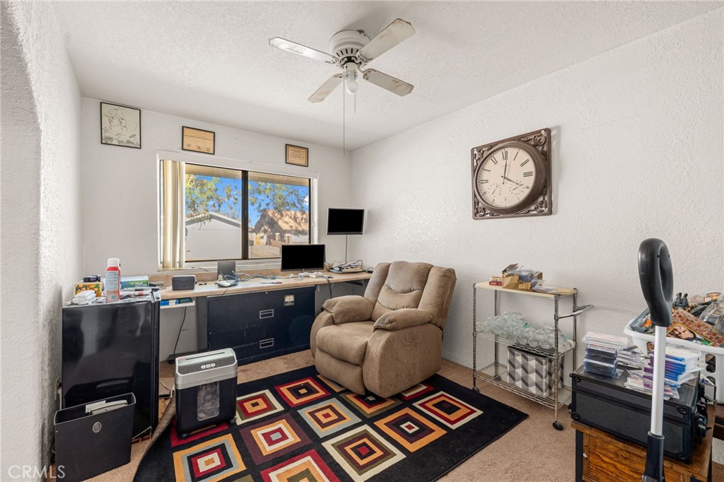 Home office with a long desk, tan recliner, ceiling fan, and colorful geometric rug.
