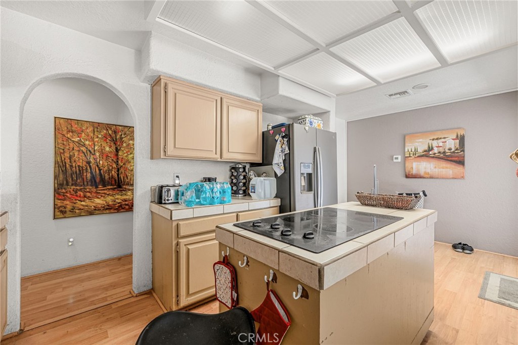Kitchen with a large cooktop island, light wood cabinets, and a stainless-steel refrigerator.