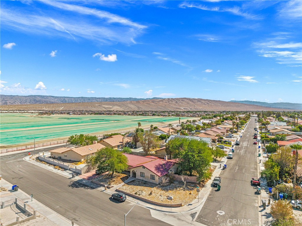 Aerial view of a corner-lot home in a desert neighborhood, with fields and distant mountains.