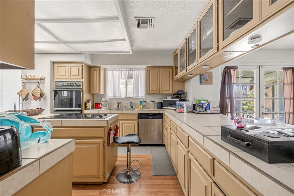 Kitchen with tan cabinets, tiled counters, central cooktop, and glass doors admitting daylight.
