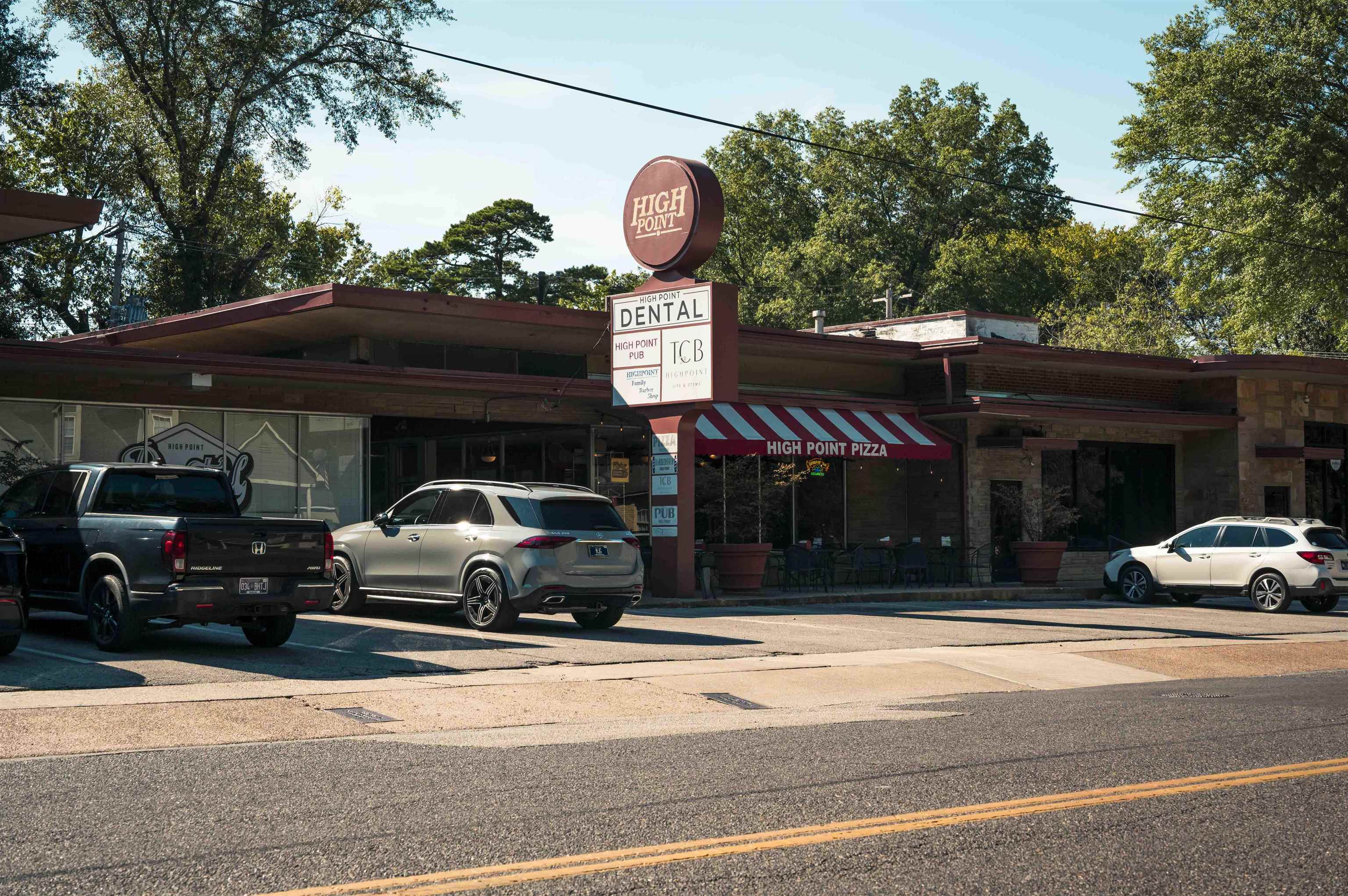 High Point Pizza storefront in a neighborhood strip with several businesses and parked cars.