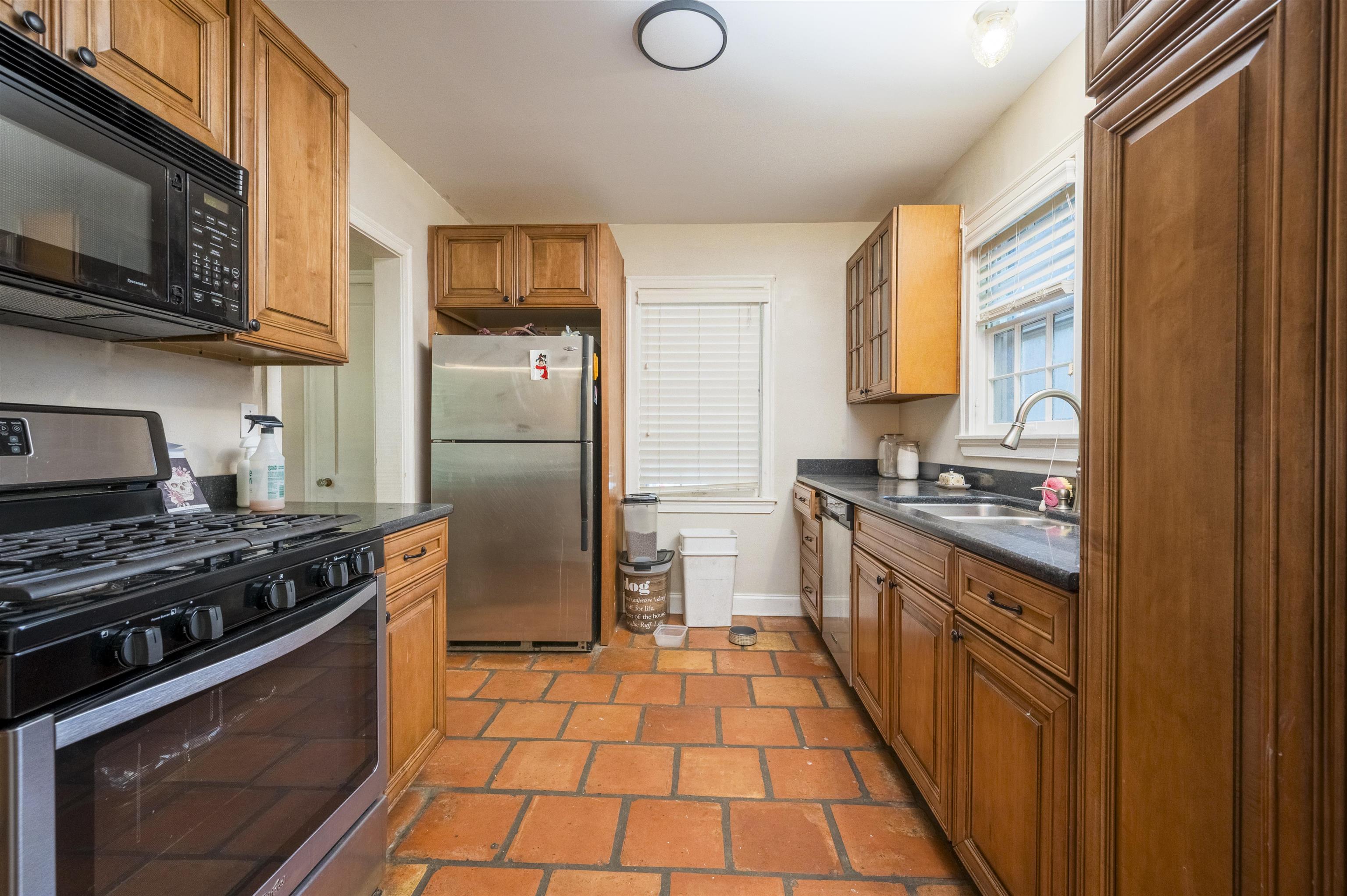 Kitchen with wood cabinets, terracotta tile floors, and stainless steel appliances.