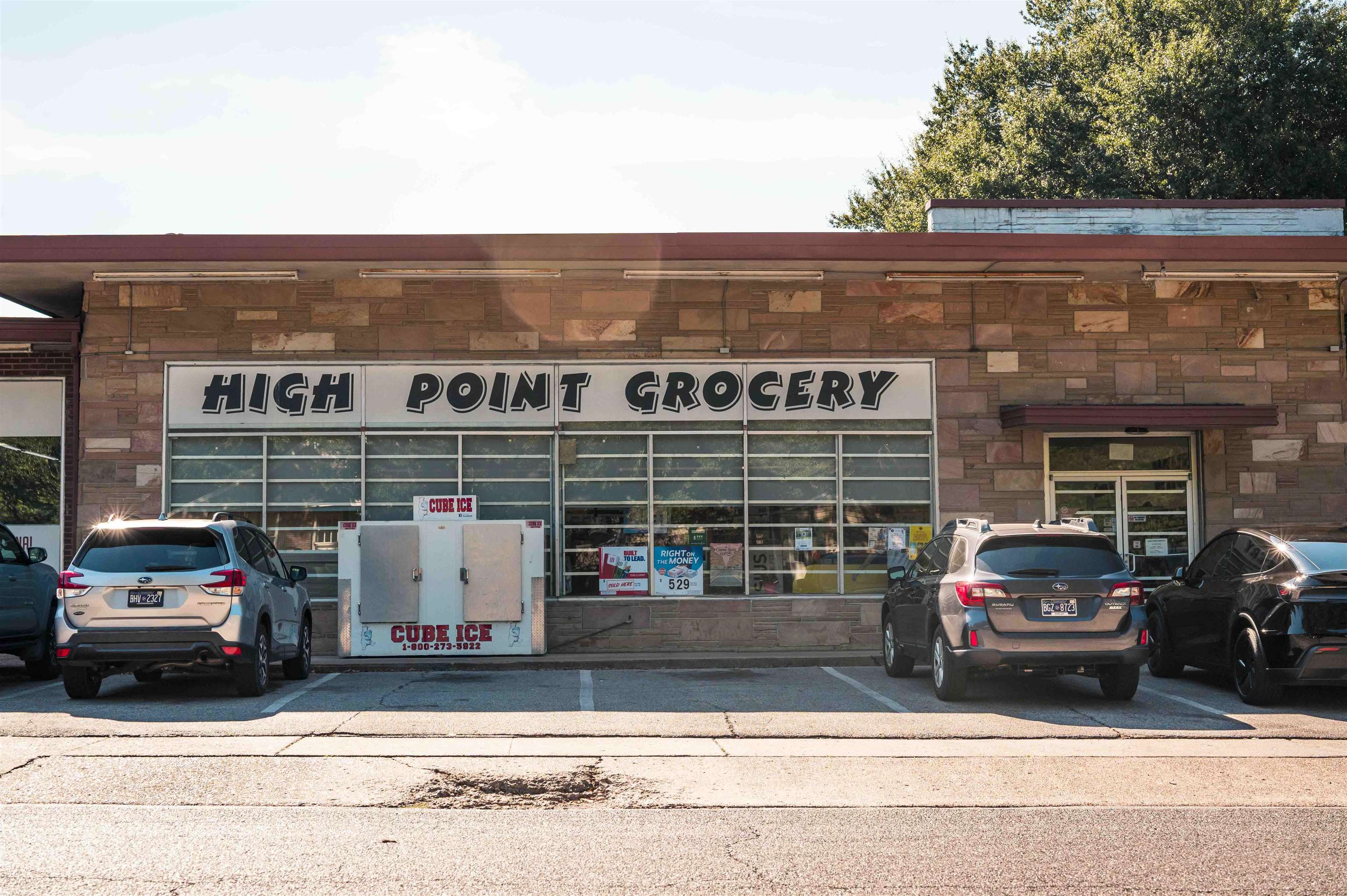 High Point Grocery storefront with a stone facade, cube ice machine, and cars parked outside.