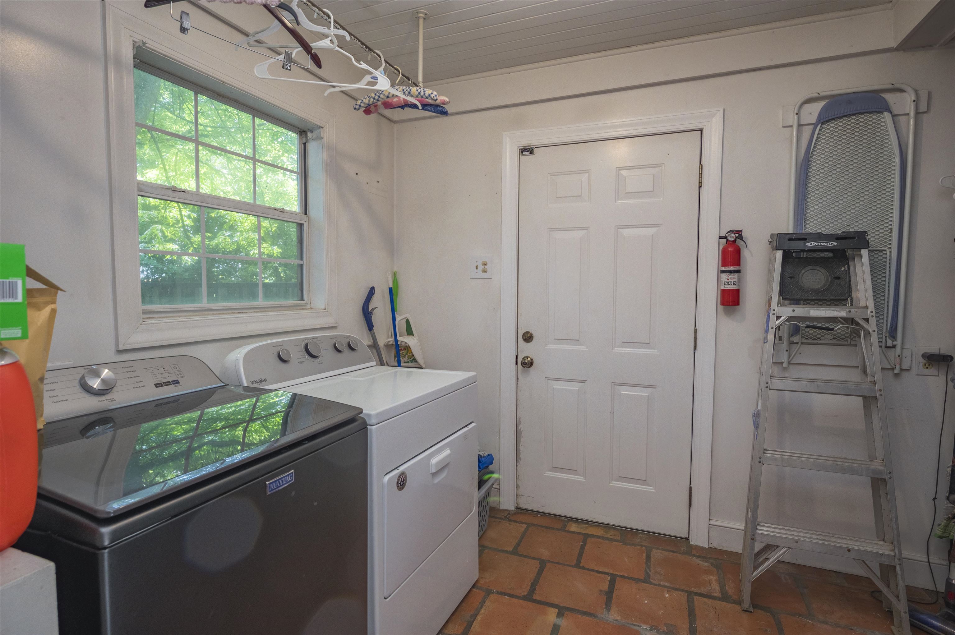 Laundry room with washer and dryer, a large window, and terracotta tile flooring.