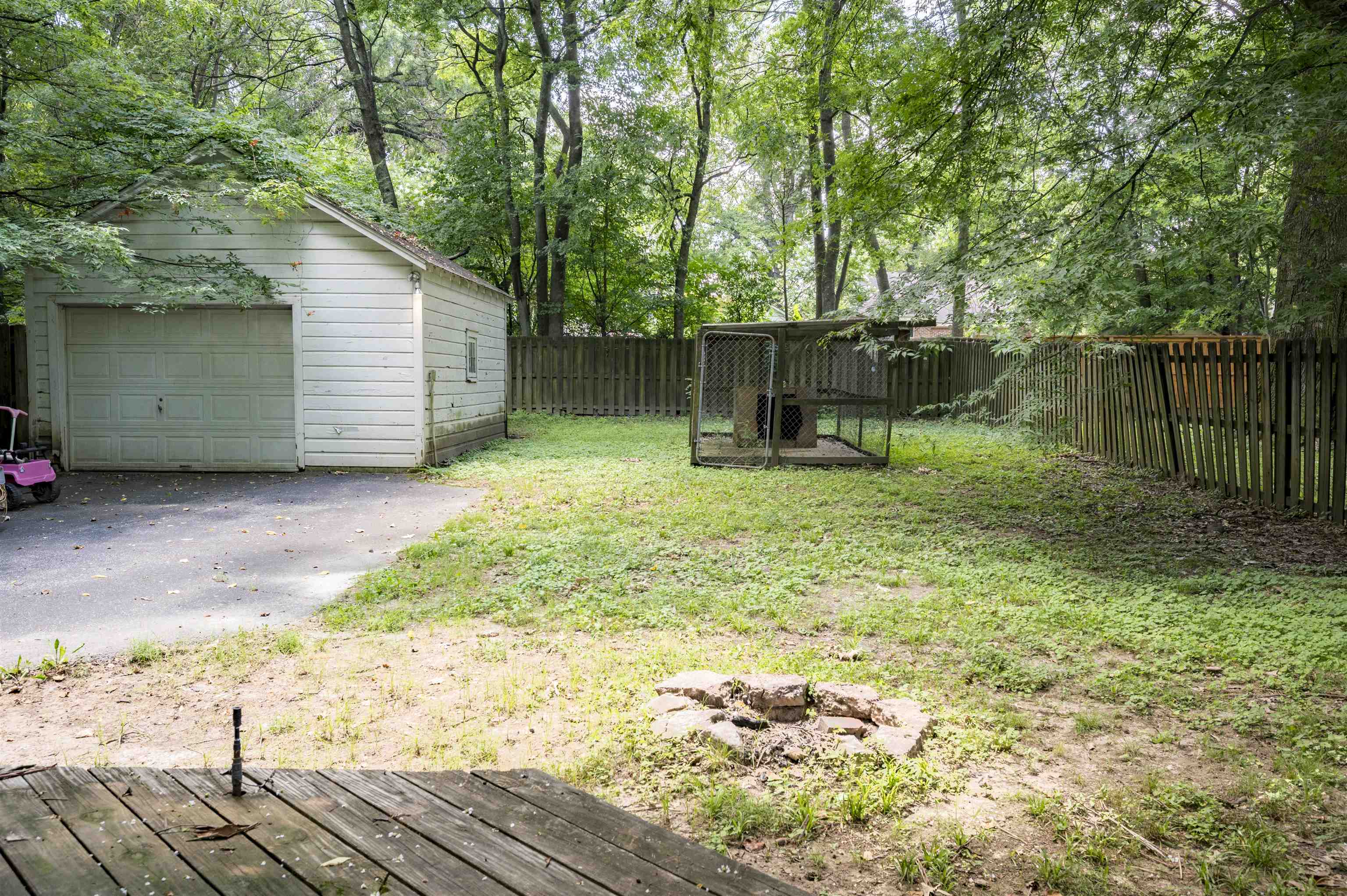 Wooded backyard with a detached garage, fenced dog kennel, and wooden deck.