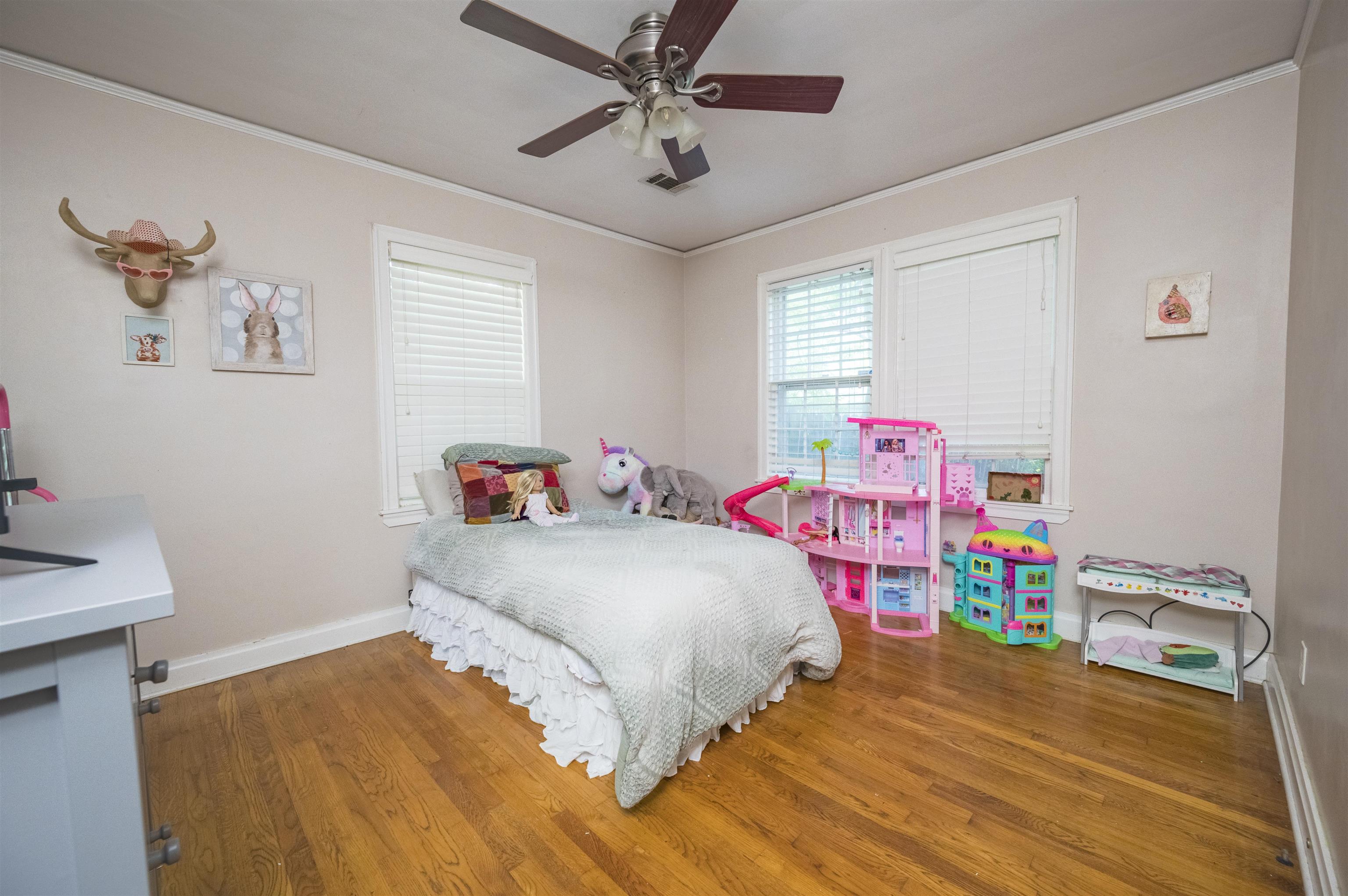 Child's bedroom with hardwood floors, a white bed, plush toys, and bright pink dollhouses.