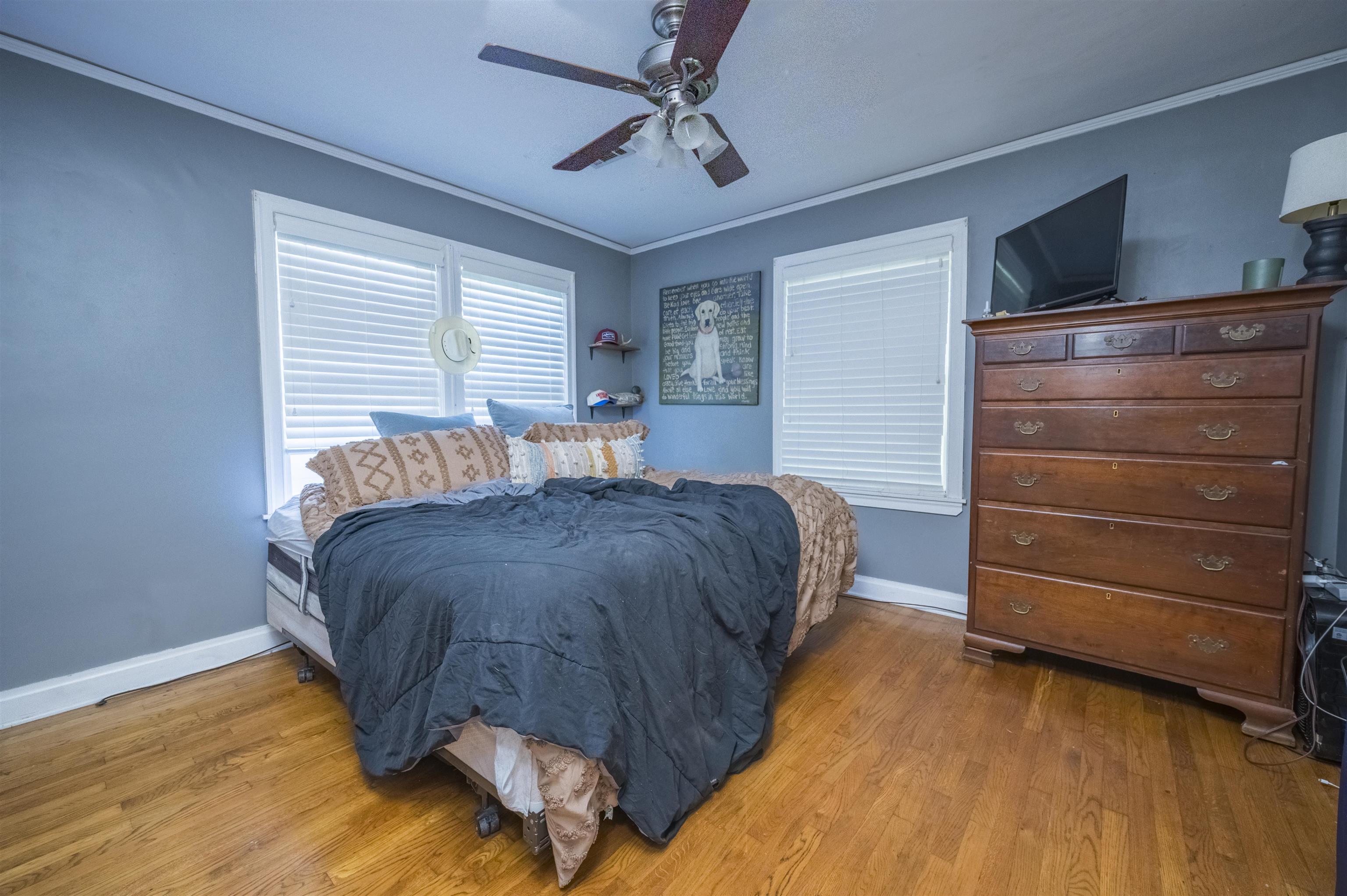 Bedroom with dark blue bedding, hardwood floors, and a tall wooden dresser beneath a television.