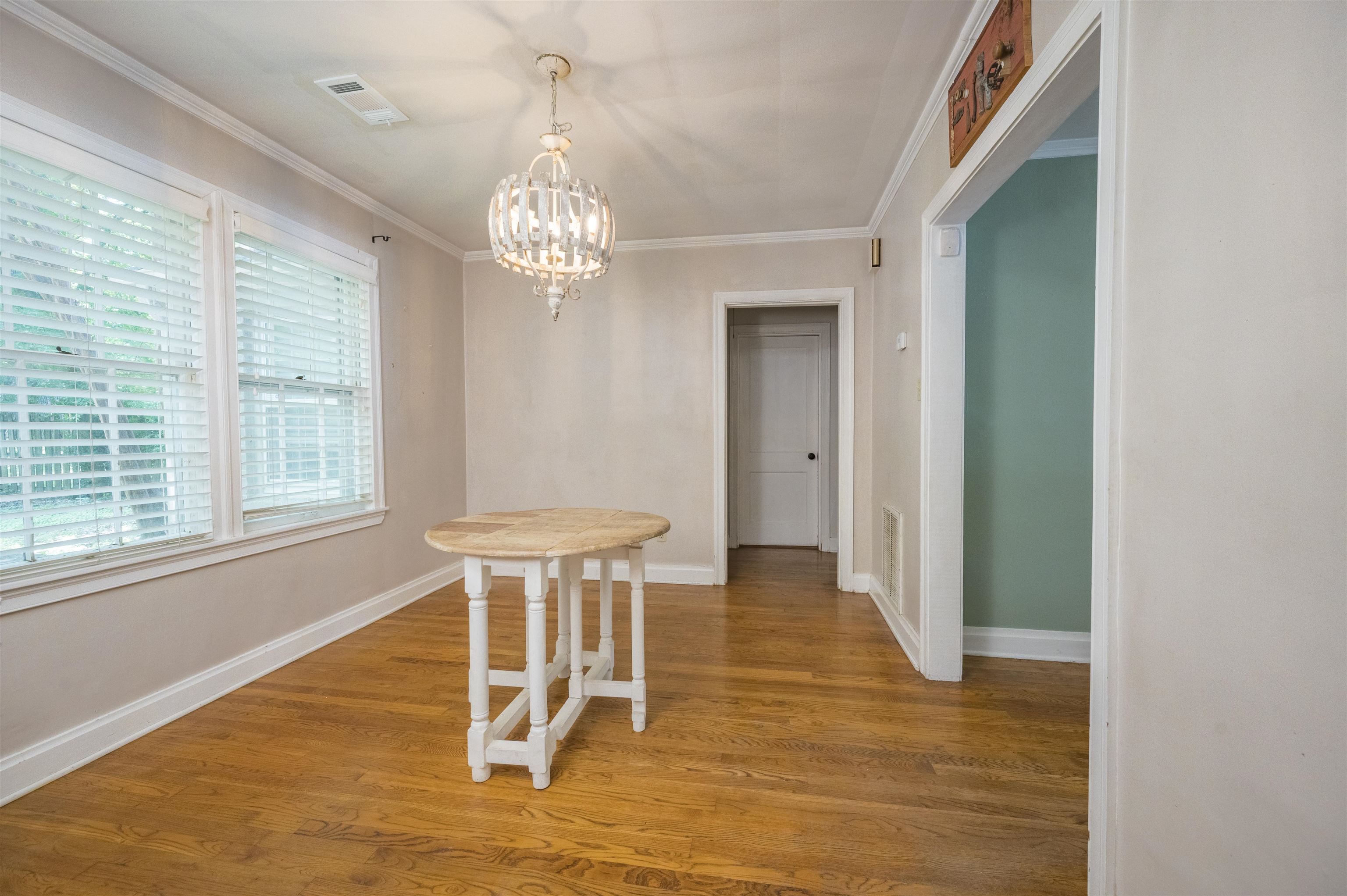 Dining room with hardwood floors, a round table, large blinded windows, and a chandelier.