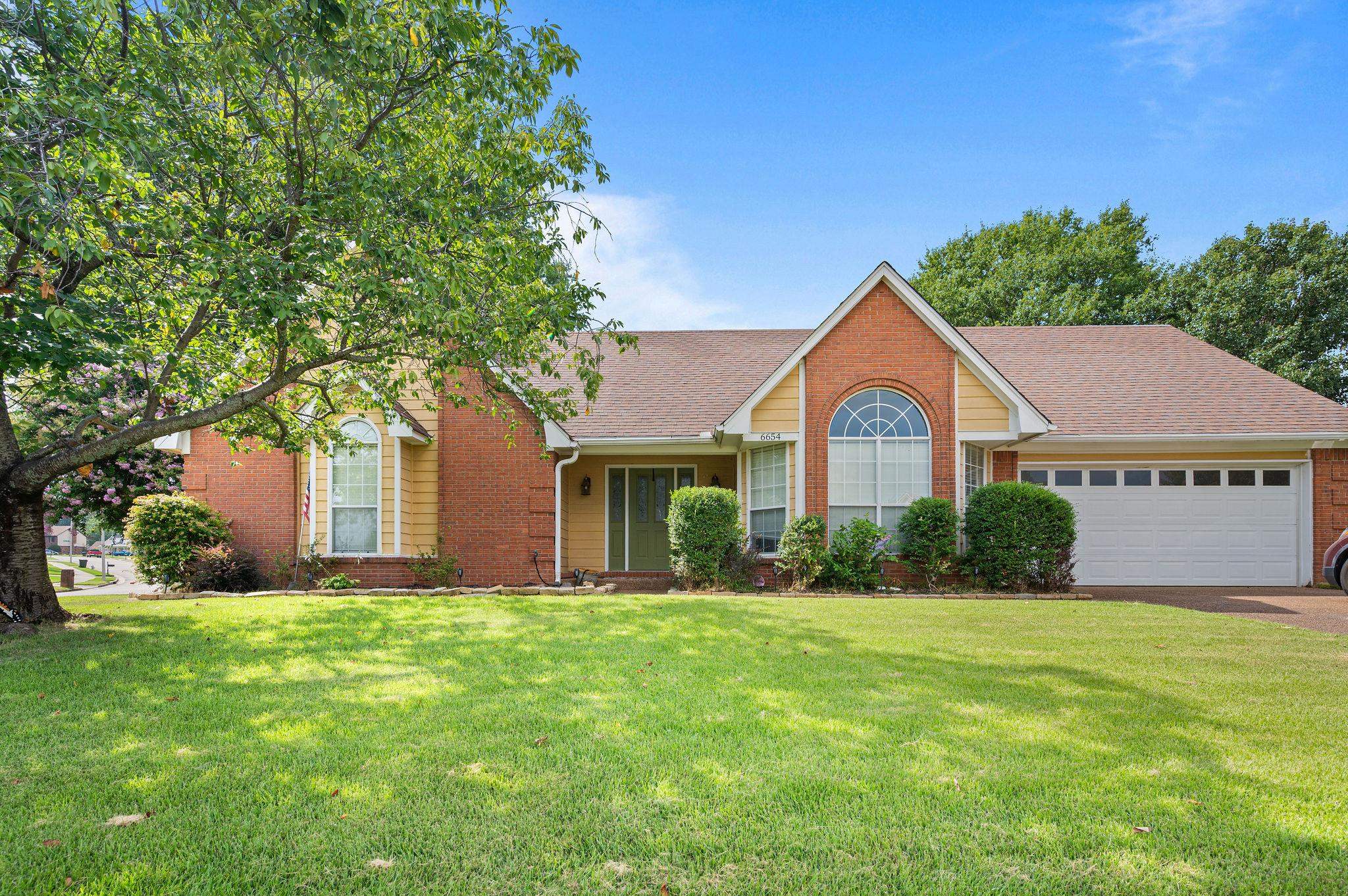 Brick-and-siding house with an arched front window, attached garage, and tree-shaded lawn.